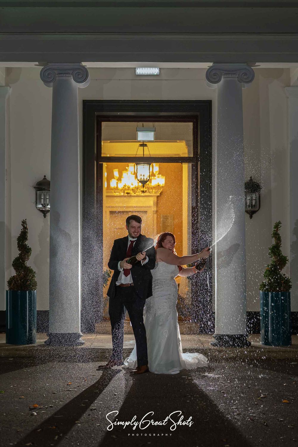 A champagne spray photograph with the bride and groom in front of the entrance to Eastwood Hall.