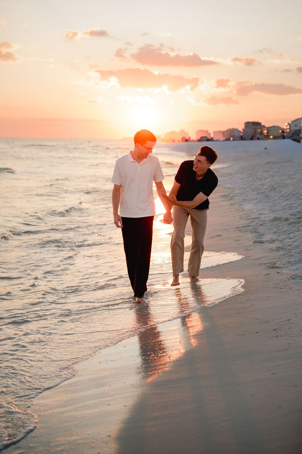 Two people walking together along a beach shoreline at sunset with golden light reflecting on the water.