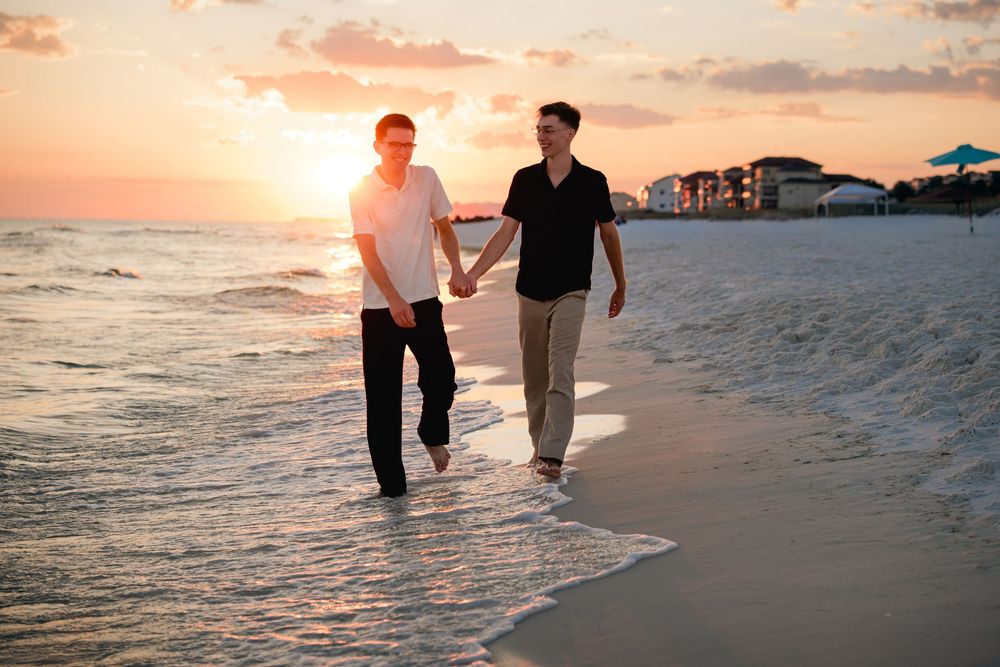Silhouetted couple walking along a beach at sunset with waves crashing on the shore.