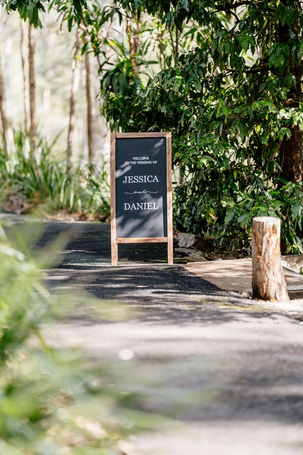 Black name signs displayed along a garden path with green foliage and trees in the background.