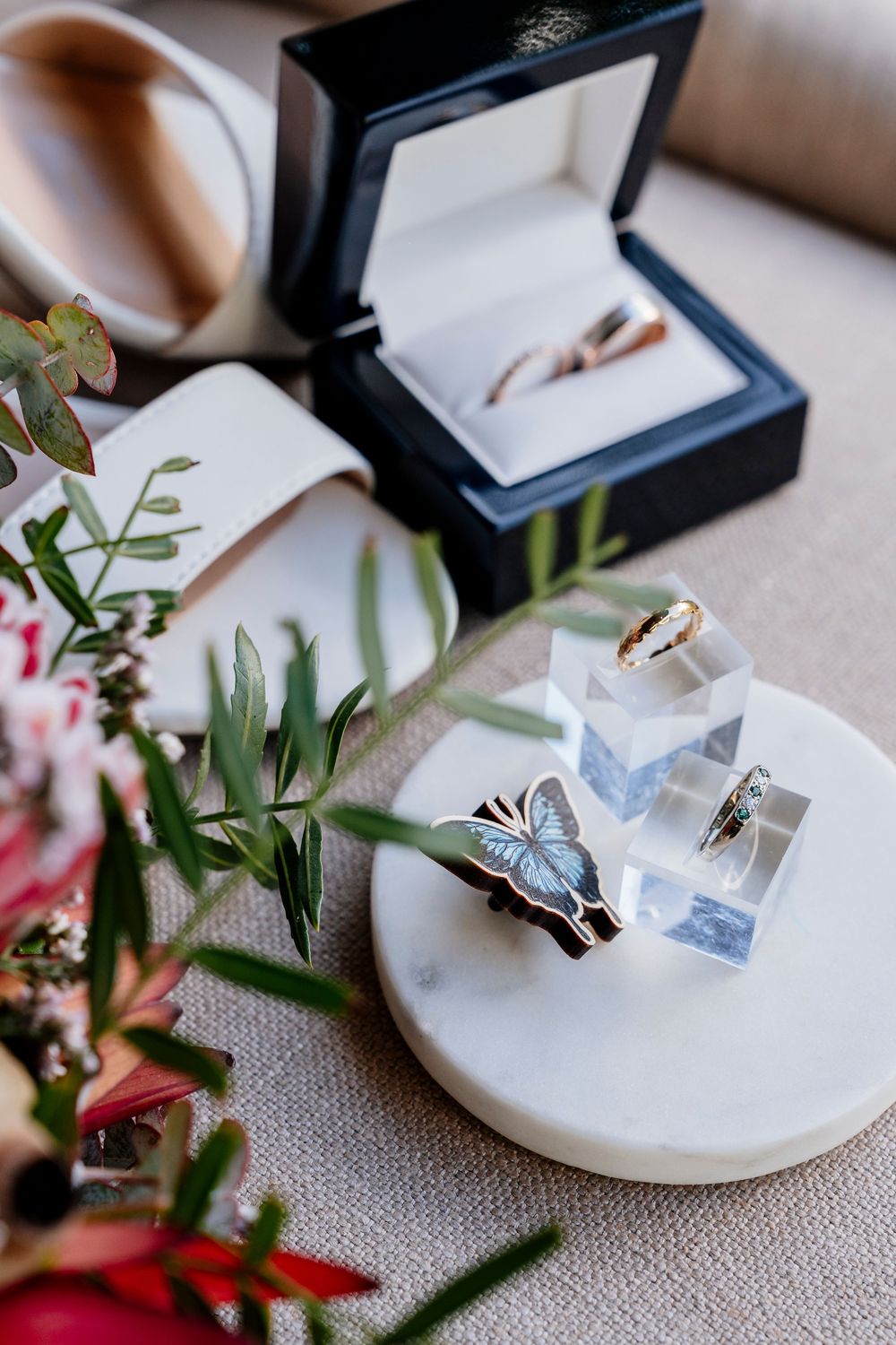Engagement rings and wedding bands displayed in navy blue ring boxes with floral decor on a textured linen surface.
