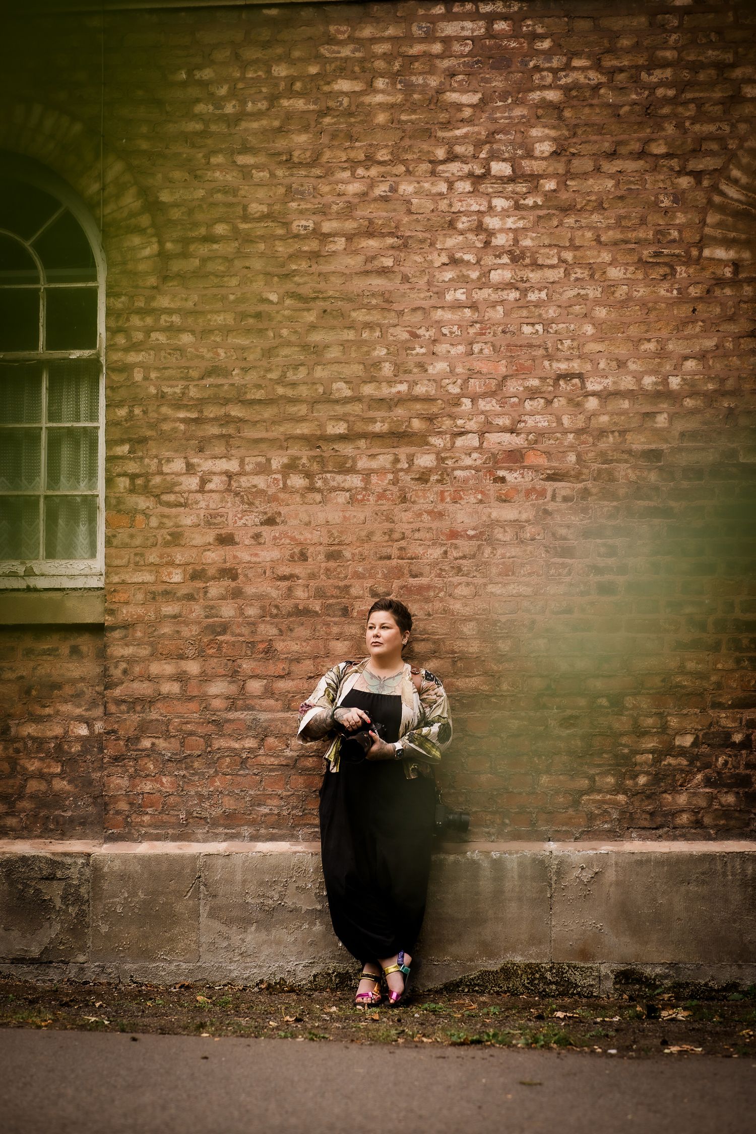 A person in black clothing sits against a rustic brick wall in a moody artistic portrait series.