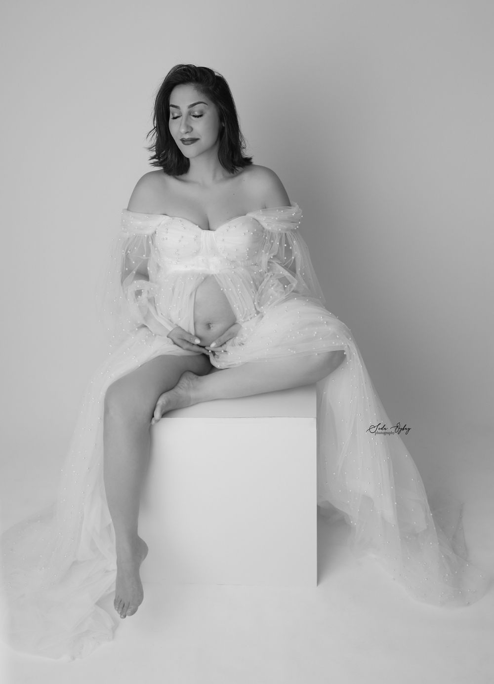 Artistic black and white maternity portrait series featuring elegant white lace gown and minimalist cube props.