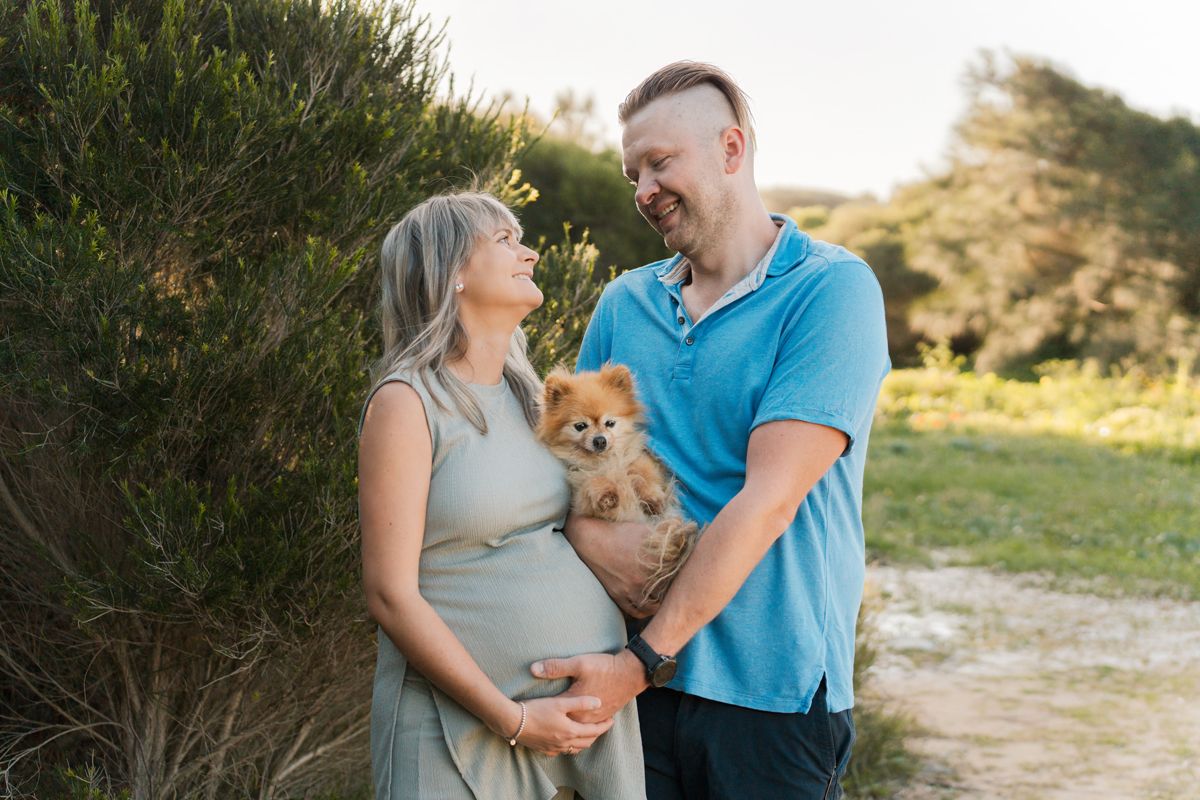 Expecting couple shares a moments including their dog during golden hour maternity photo session in a natural outdoor setting in Maroubra