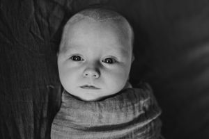 Black and white portrait of an infant against a dark background.