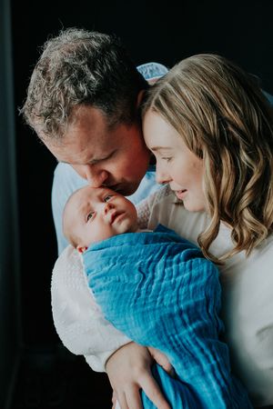 Intimate family moment with newborn baby wrapped in blue blanket.