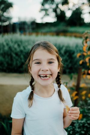 Young child with braided hair smiling outdoors in a garden setting.