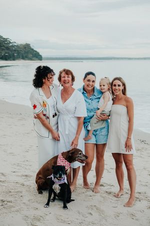 Group gathered on beach with dog wearing bandana in foreground.