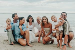 Extended family group photo on sandy beach with ocean backdrop.