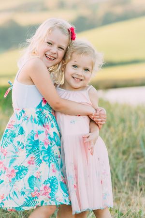 Two young children in floral summer dresses playing in a sunny field.