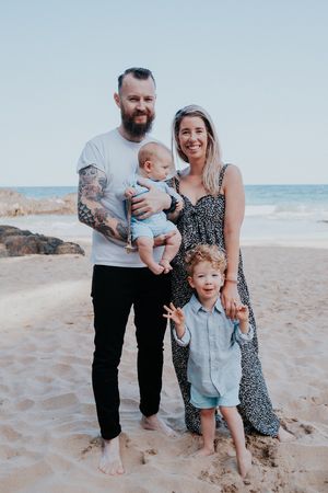 Family enjoying a playful moment together on a sunny beach with ocean waves in the background.