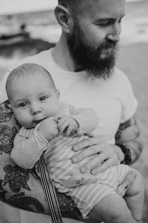 Black and white close-up shots of a baby being held with tattooed arms visible.