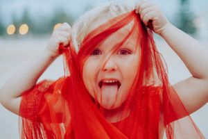Playful portraits with person wearing bright red fabric against light background.
