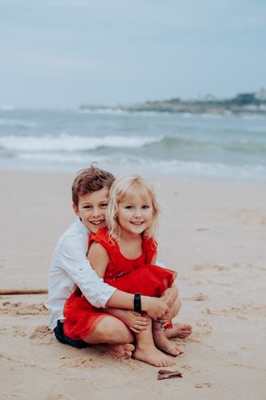 Children playing together on a sandy beach wearing red and white outfits.