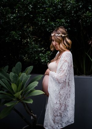 Maternity photos in a garden setting featuring white lace dress against dark foliage.