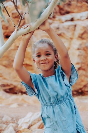 A child in a blue dress plays joyfully outdoors near rocky formations.