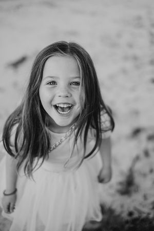 A laughing child in a white dress with flowing dark hair captured in black and white.