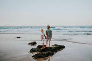 Family enjoying a sunset walk along a rocky beach coastline during golden hour.