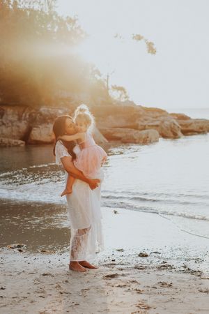 Romantic beach photoshoot at sunset with couple embracing on sandy shore.