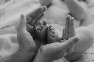 Close-up black and white photo of tiny baby hands reaching upward against a light background.