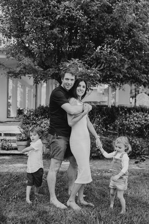 Black and white photo of family playing and jumping together in a park setting.