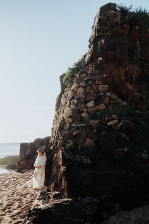 Couple standing near dramatic rocky cliff formation on beach at sunset.