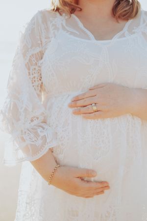 Series of gentle hands cradling a pregnant belly in white lace dress.