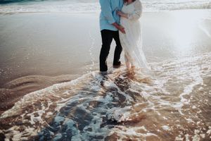 Couple walking together in shallow ocean waves at sunset.