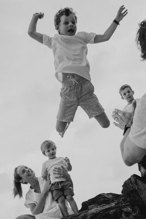 Joyful black and white photos capturing children being tossed in the air against a bright sky.