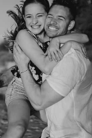 Black and white photos capture candid moments of a family laughing and hugging at the beach.