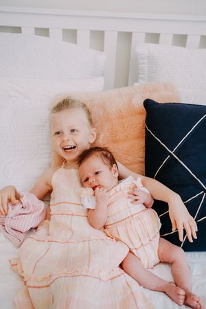Two young children in matching outfits share sweet giggles while lying on a bed.