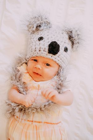 Baby wearing an adorable knit animal hat poses on white bedding.