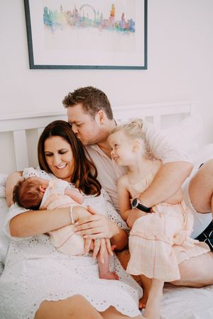 Candid lifestyle photos of a family sharing tender moments on a bed with artwork in background.