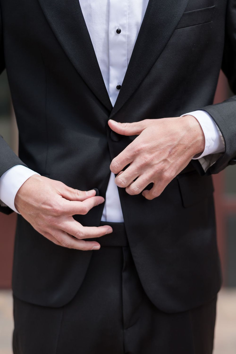 Close-up shots of hands adjusting formal black tuxedo jacket and white dress shirt.