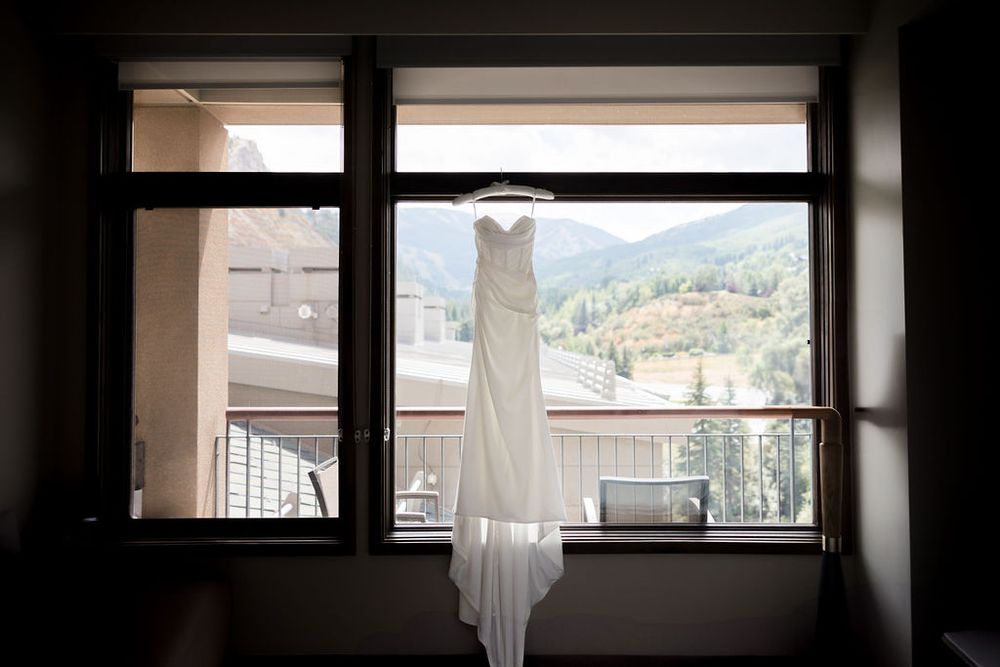 Wedding dress hangs in silhouette against large windows with mountain views.