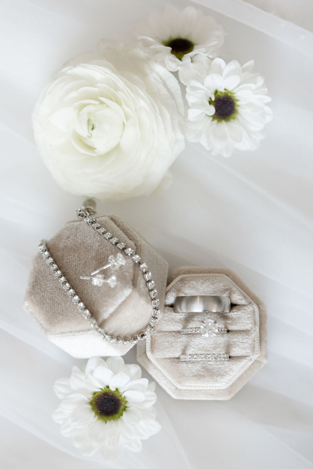 White flowers and wedding rings displayed on light fabric.