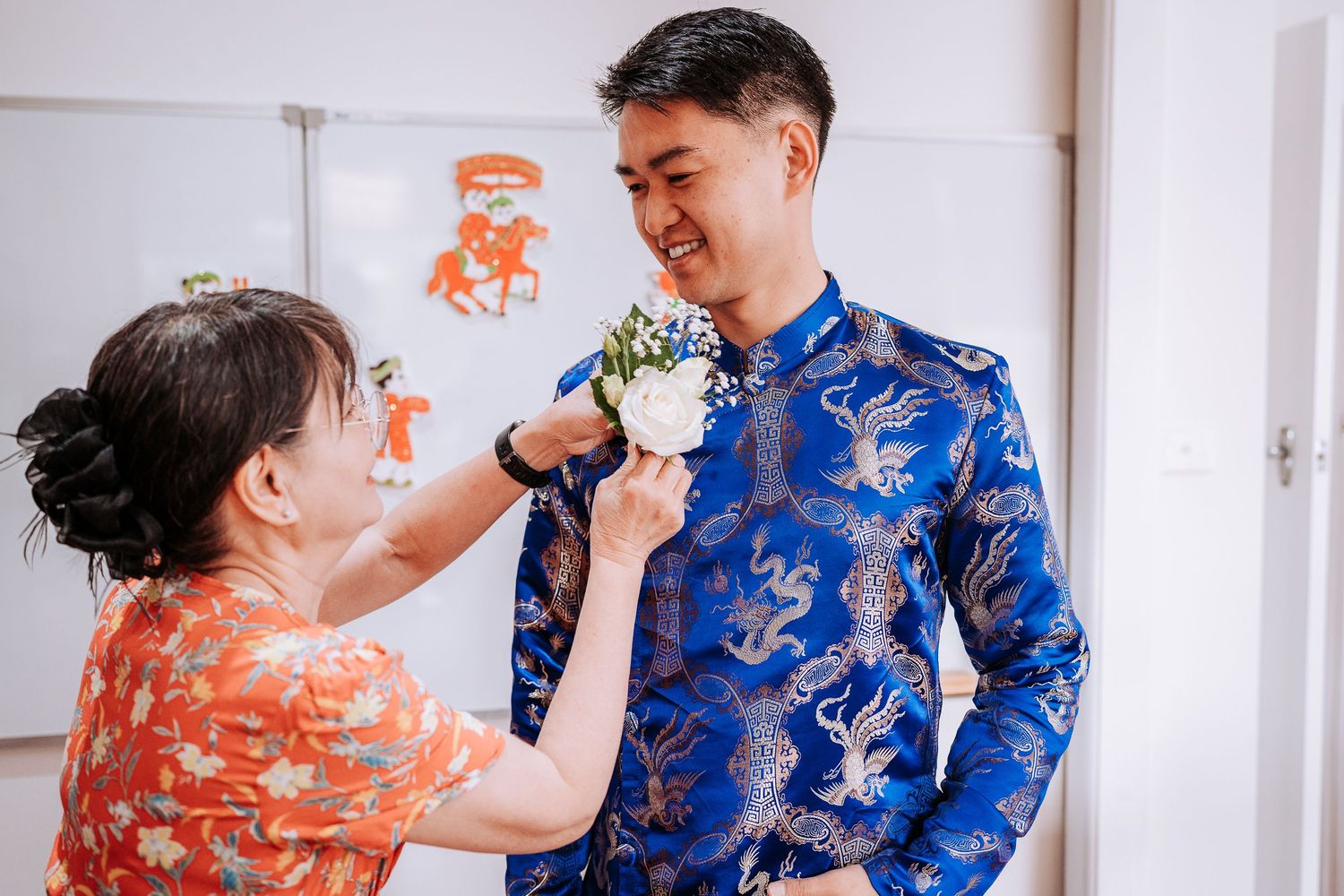 Couple in traditional Chinese wedding attire playfully feeding each other cake during a tea ceremony celebration.