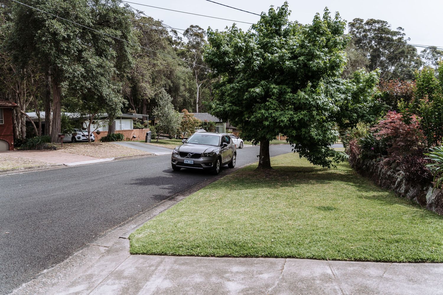 Residential street view with parked car and well-maintained front lawn.