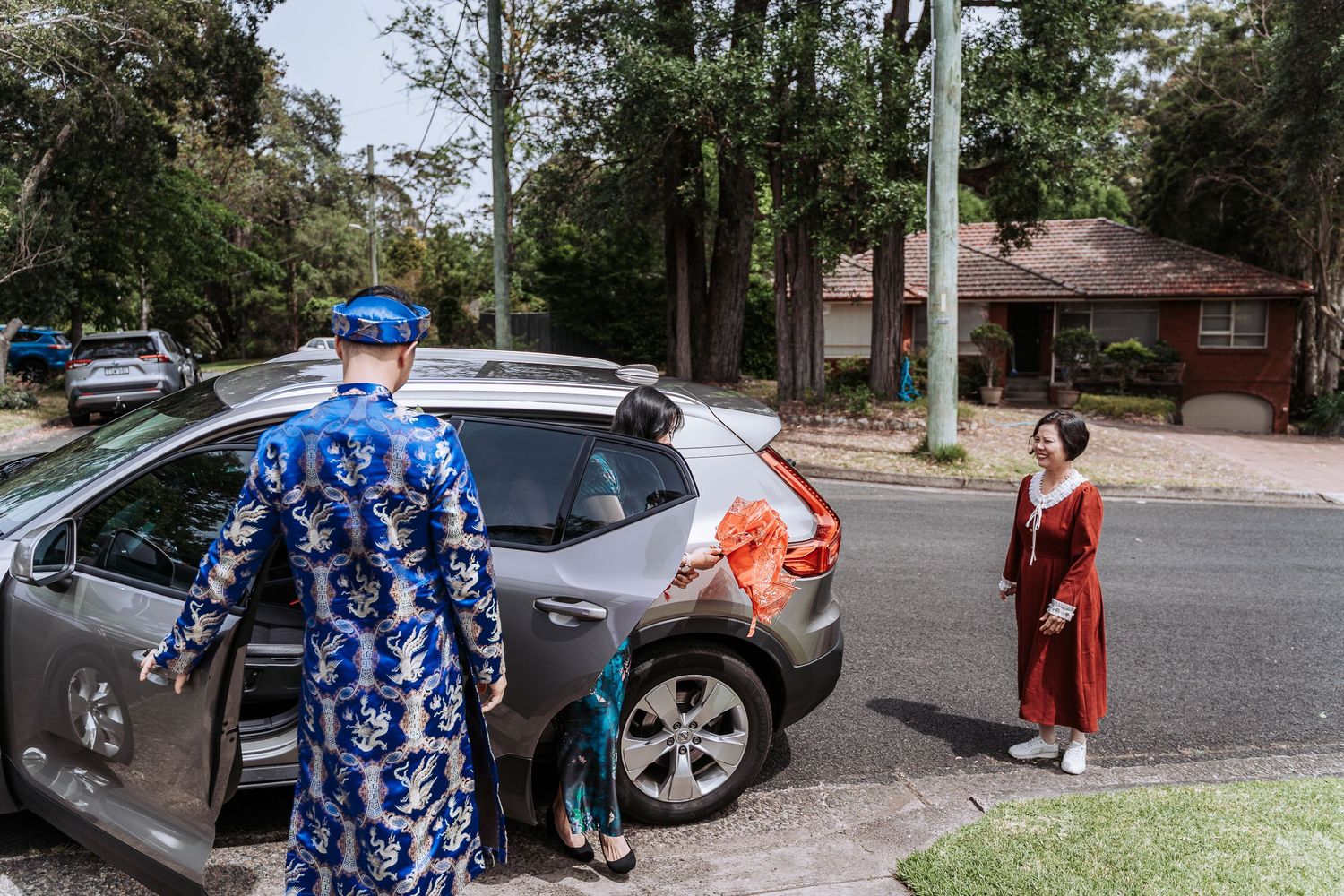 People in formal attire walking through a parking lot on a sunny day.