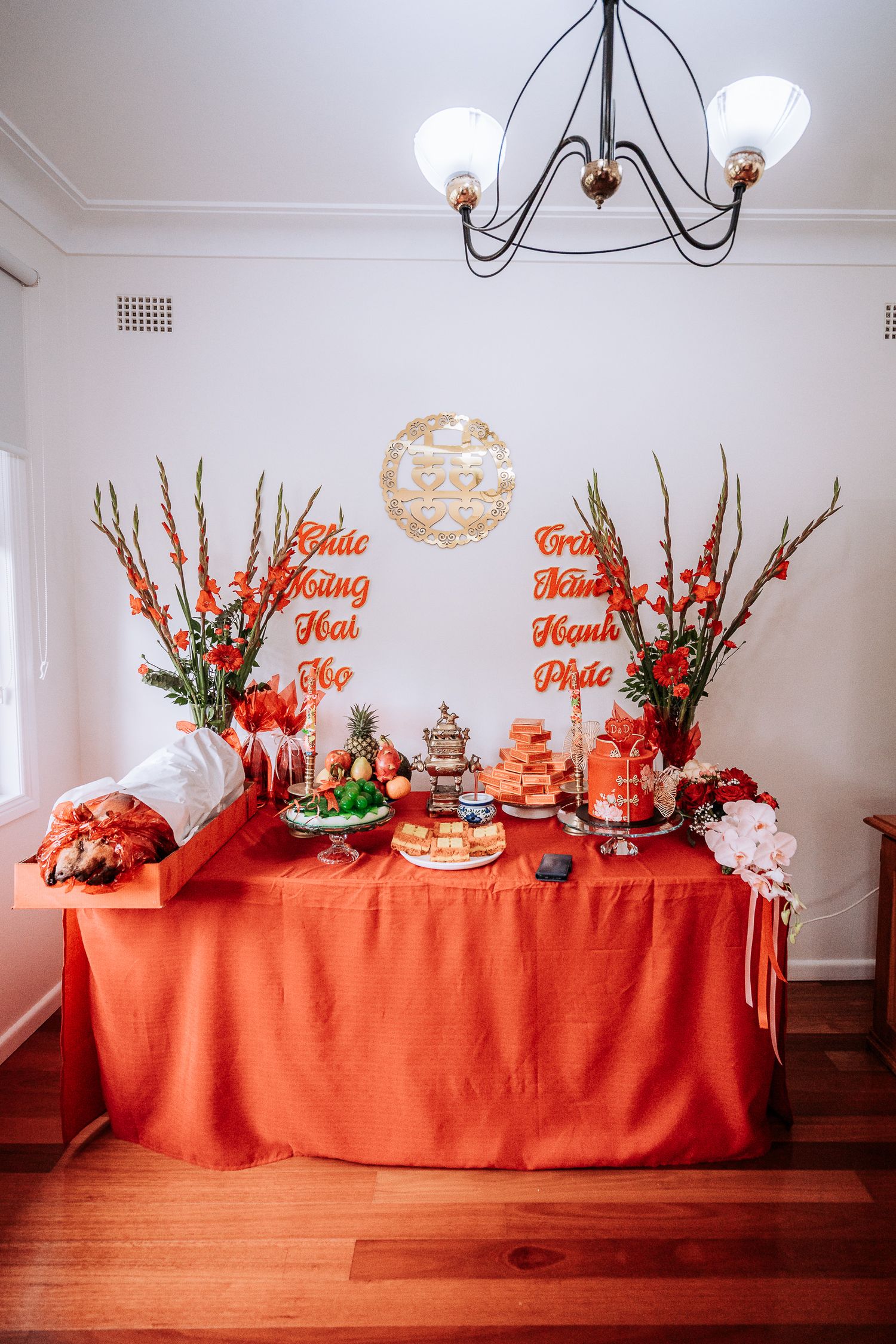 Festive party table decorated with bright orange tablecloth, floral arrangements and desserts for a special celebration.