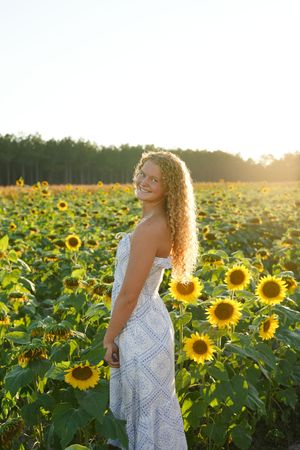 Candid portrait session in a blooming sunflower field during sunset with white floral dress.