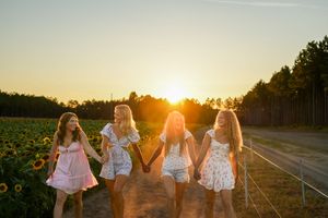 Friends holding hands while walking through a sunflower field during golden hour.