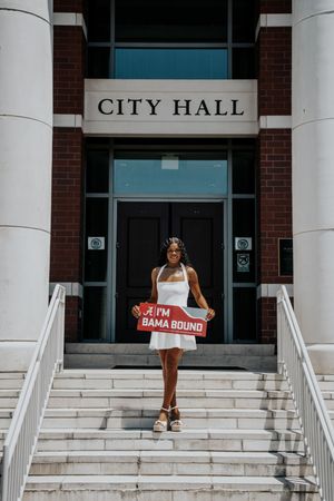 Young woman holding an 'I'm Bama Bound' sign on City Hall steps, celebrating her University of Alabama commitment.