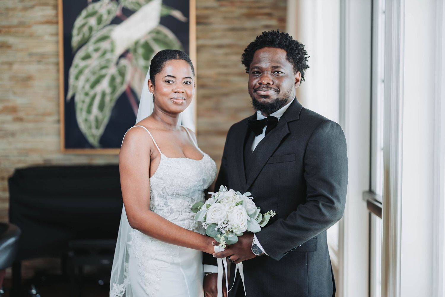 A happy couple on their wedding day wearing formal attire and holding a white floral bouquet.