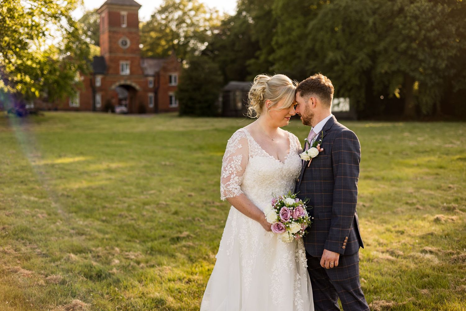 Newlyweds share an intimate moment at sunset with a historic brick building in the background.