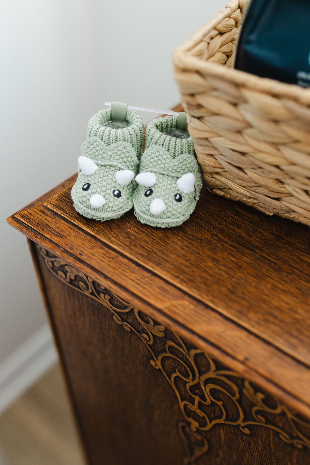 Mint green knitted baby booties with cute animal faces displayed on a rustic wooden surface.