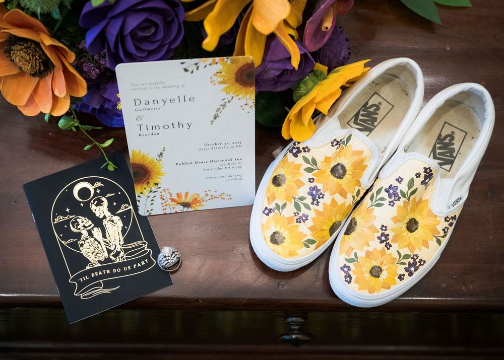 Wedding invitation suite with purple and yellow floral details alongside white flip flops.