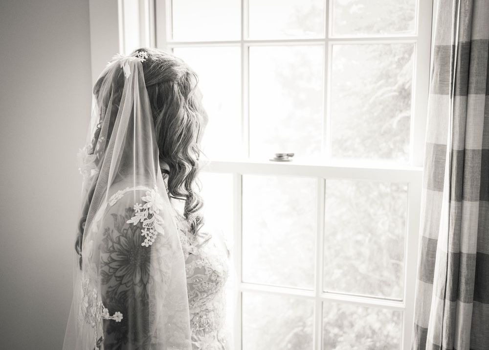 A delicate lace wedding veil hangs by a sunlit window creating a dreamy silhouette.