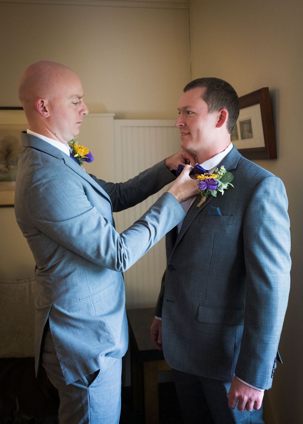 A sequence of photos showing a groomsman helping adjust another's boutonniere in a light blue suit.