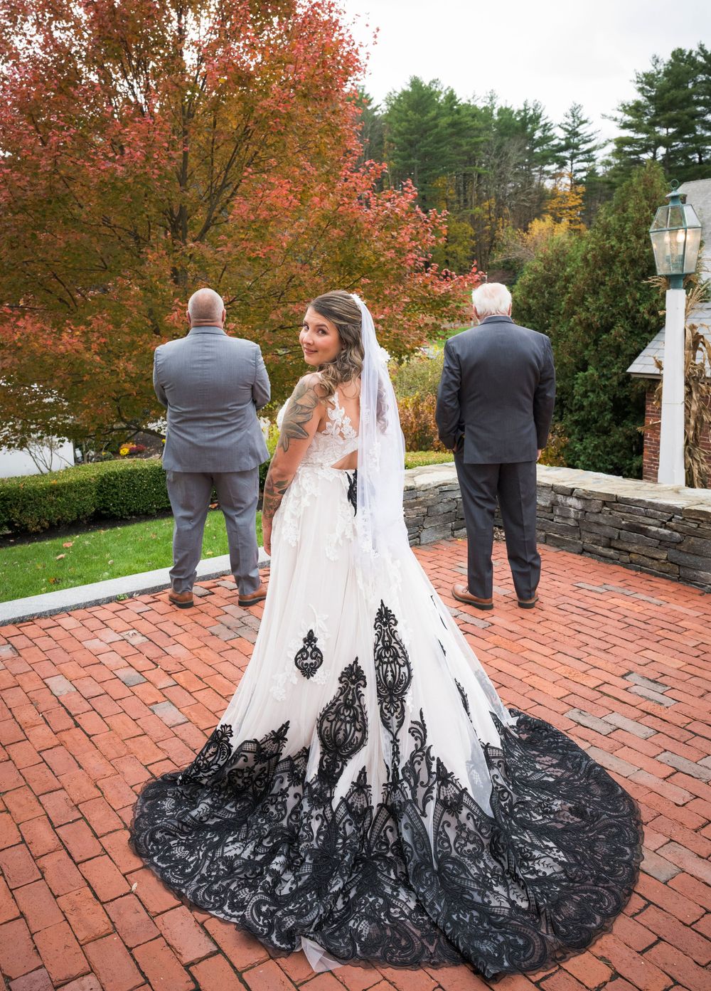 A stunning white wedding dress with black lace details photographed from behind against autumn foliage.